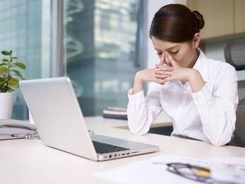 asian businesswoman sitting in office, looking tired.