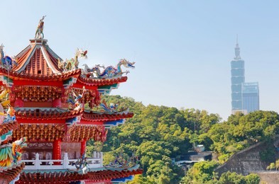 view of the colorful eaves of a taiwanese temple decorated   in traditional mosaic art and buildings  in background in taipei city, taiwan