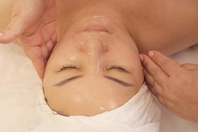 portrait of a woman of asian appearance receiving a wellness massage of the face. close-up. a woman with closed eyes lies on the couch at the beautician. shooting from above