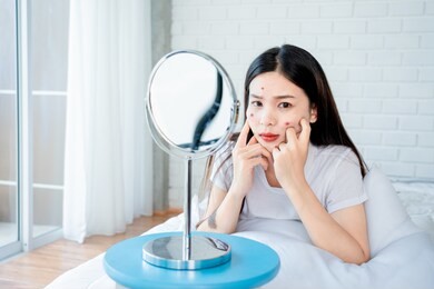 asian teenage woman  looking at mirror and squeeze acne problem on her face, skin care concept.