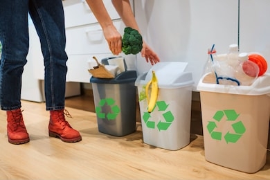 waste sorting at home. cropped view of woman putting broccoli in the garbage bin. colorful trash bins for sorting waste in the kitchen