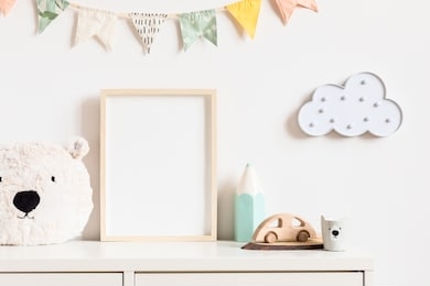 stylish and modern scandinavian newborn baby interior with mock up photo or poster frame on the white shelf. toys, teddy bear, wooden car and hanging cotton colorful flags and star. template. blank.