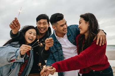 diverse group of young people celebrating new year's day at the beach. young asian people having fun with sparklers outdoors at the sea shore.