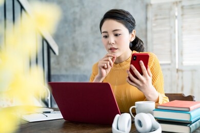 young asian woman using a laptop computer and a smart phone.