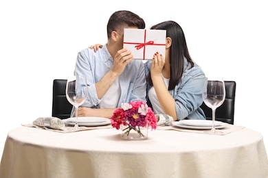 young male and female hiding behind a gift box at a restaurant table isolated on white background