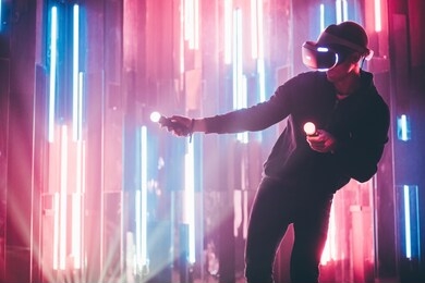 young man using joystick in hands and vr headset on head playing in dark space on background colored neon lights.