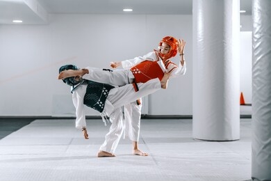 two caucasian boys in taekwondo fittings kicking and fighting at training.