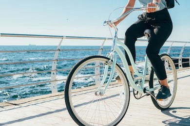 young woman riding vintage bike along the waterfront. female traveler with backpack cycling near sea on sunny summer day.