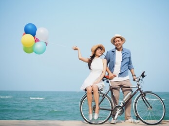 happy young asian couple lover holding colorful of balloons over blue sky background,they ‘re spend the time for travel at tropical beach together in summer vacation time.
