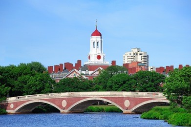 john w. weeks bridge and clock tower over charles river in harvard university campus in boston with trees and blue sky.