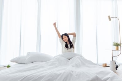 asian woman wake up in the morning, sitting on white bed and stretching, feeling happy and fresh