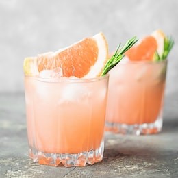 drink rosemary grapefruit and ice glass goblet on a light gray concrete background. refreshing summer cocktail close-up.