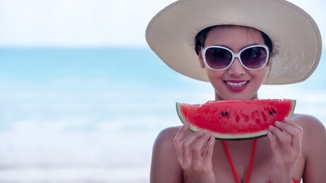 beautiful young asian woman wear sunglasses and hat happy, smile with watermelon while relaxing on beach on summer holidays. concept freedom, lifestyle, tourism, holiday. with copy space