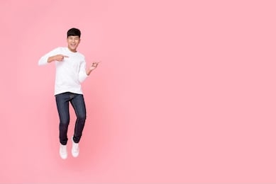 young cheerful energetic handsome asian man jumping with hands pointing to copy space aside studio shot isolated on pink background