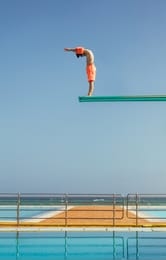 boy stands on a diving platform about to dive into the swimming pool. boy standing on high diving spring board preparing to dive.
