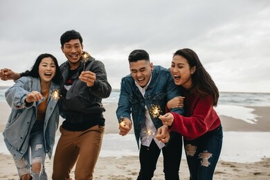 group of asian friends having fun with sparklers at the beach. group of young men and women celebrating new year's day at the beach.
