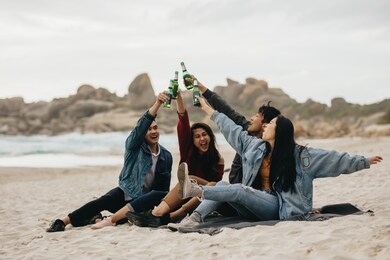excited four asian friends toasting beer on the beach. young people on the beach having a party with drinks.