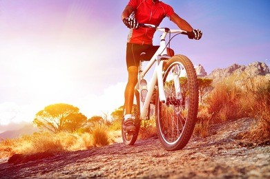 low angle view of cyclist riding mountain bike on rocky trail at sunrise