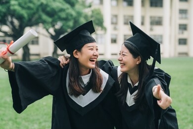 graduation asian female friends hold diploma. cheerful ladies students hugging shoulders arms with thumb up finger hand gesture best sign. beautiful cheerful women students looking each other smiling