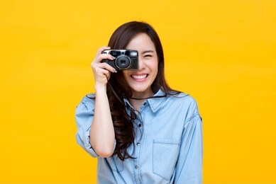 cute amateur young asian woman photographer smiling and taking picture on colorful yellow studio background