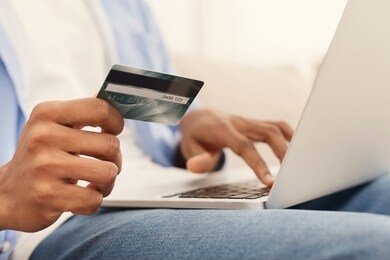 black millennial guy shopping in internet on laptop, using credit card to pay, closeup