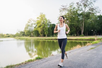healthy beautiful young asian runner woman in sports clothing running and jogging on sidewalk near lake at park in the morning. lifestyle fitness and active women exercise in urban city concept.