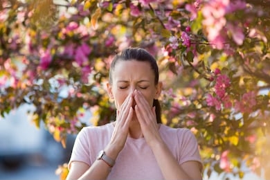 young pretty woman sneezing in front of blooming tree. spring allergy concept