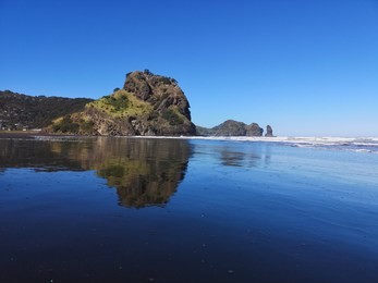 piha beach, auckland, new zealand - sep 9th, 2018. the reflection of a rock on the black sands of piha beach in auckland, new zealand on september 9th, 2018.