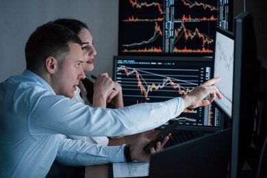 works at evening. team of stockbrokers are having a conversation in a office with multiple display screens.
