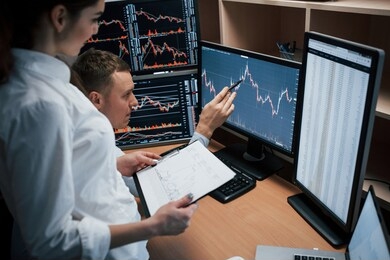 business don't do itself, you need to struggle to achieve good results team of stockbrokers are having a conversation in a office with multiple display screens.