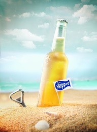 capped bottle of chilled fruity orange soda or ale (beer) standing in the golden sand on a tropical beach with a bottle opener and skipper sign. look at my portfolio for more cocktails.