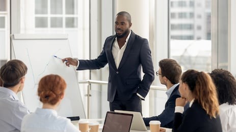 african american conference speaker coach talk to audience give presentation on flipchart to employees group, black trainer manager speaking training diverse corporate team at office meeting seminar
