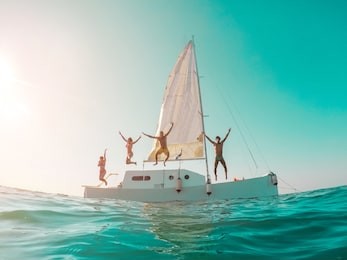 happy crazy friends diving from sailing boat into the sea - young people jumping inside ocean in summer vacation - main focus on left girls - travel and fun concept - fisheye lens distortion