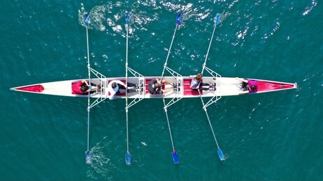 aerial drone bird's eye view photo of red sport canoe operated by team of young men and women in emerald clear sea