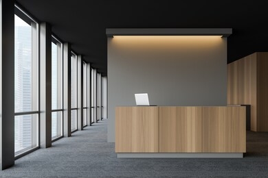 front view of wooden reception desk with laptop computer on it standing in modern company office with dark gray walls and carpeted floor. 3d rendering