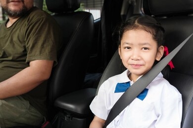 asian girl wear uniform sit in the car and fasten the belt for safety. the students sitting with the parents going to school.