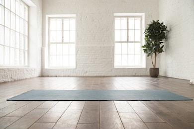 unrolled yoga mat on wooden floor in modern fitness center or at home with big windows and white brick walls, comfortable space for doing sport exercises, meditating, yoga equipment