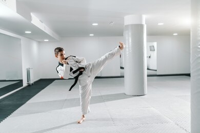 caucasian boy in dobok kicking in dollyo-chagi pose. taekwondo training concept.