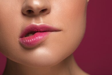 close up photo of the thoughtful woman with pink lip gloss biting her lip while being isolated on the maroon background