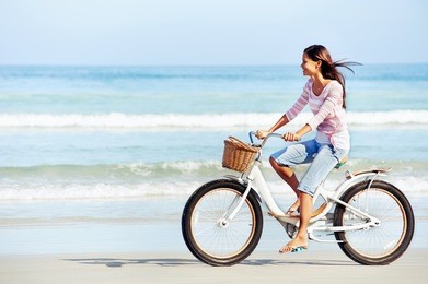carefree woman with bicycle riding on beach sand having fun and smiling