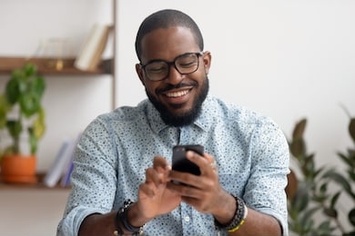 happy african american businessman using phone mobile corporate apps at workplace texting sms, smiling black man looking at smartphone browsing internet, office technology and digital communication