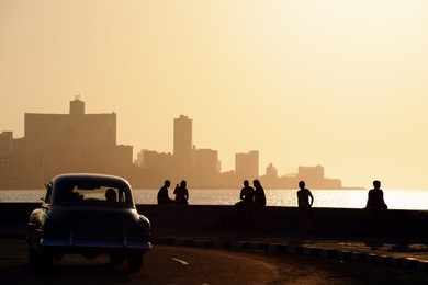 skyline in la habana, cuba, at sunset, with vintage cars on the street and people sitting on the malecon. copy space
