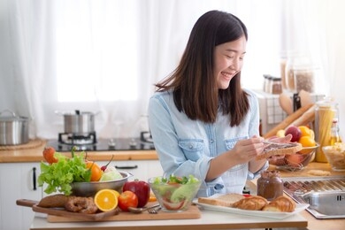 young asian woman apply jam on bread, and preparing a breakfast in the kitchen