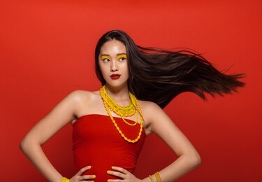 attractive woman with stylish stage make up and hair flying on red background. asian female model with creative make up and accessories.