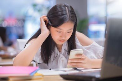 portrait of young asian female student using her mobile phone sending a text outside at cafe.