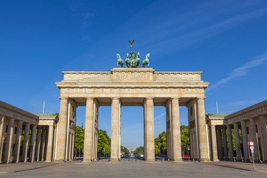 sunlight illuminating brandenburg gate (1788) inspired by greek architecture, built as a symbol of peace and nationalism, now an emblem of reunification.