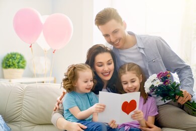 happy mother's day! children daughters with dad congratulating mom and give her flowers, gift and card. family holiday and togetherness.
