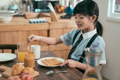 peanut butter sandwich toast bread on wooden table kitchen at home morning. smiling happy little kid elementary school student in uniform before study eating breakfast. cute child having healthy meal