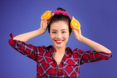 healthy food. smiling lovely pinup asian girl holding orange over blue background.