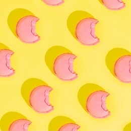 pattern of pink bitten macaroons or almond cookies on yellow background with strong shadows